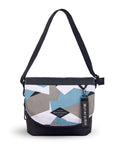 Flat front view of Sherpani crossbody, the Milli in Summer Camo. The messenger style bag is two-toned: the layover flap is a camouflage pattern of light blue, gray and white, the remainder of the bag is black. Easy-pull zippers are accented in black. The bag has an adjustable crossbody strap. A branded Sherpani keychain is clipped to a fabric loop in the upper right corner.