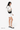 Model wearing the Sherpani crossbody, the Milli in Con Leche, holding the strap and standing sideways #color_con-leche