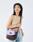 Close up view of a dark haired model facing the camera and smiling. She is wearing a beige crop top and jeans. She carries Sherpani crossbody, the Milli in Lavender, over her shoulder.