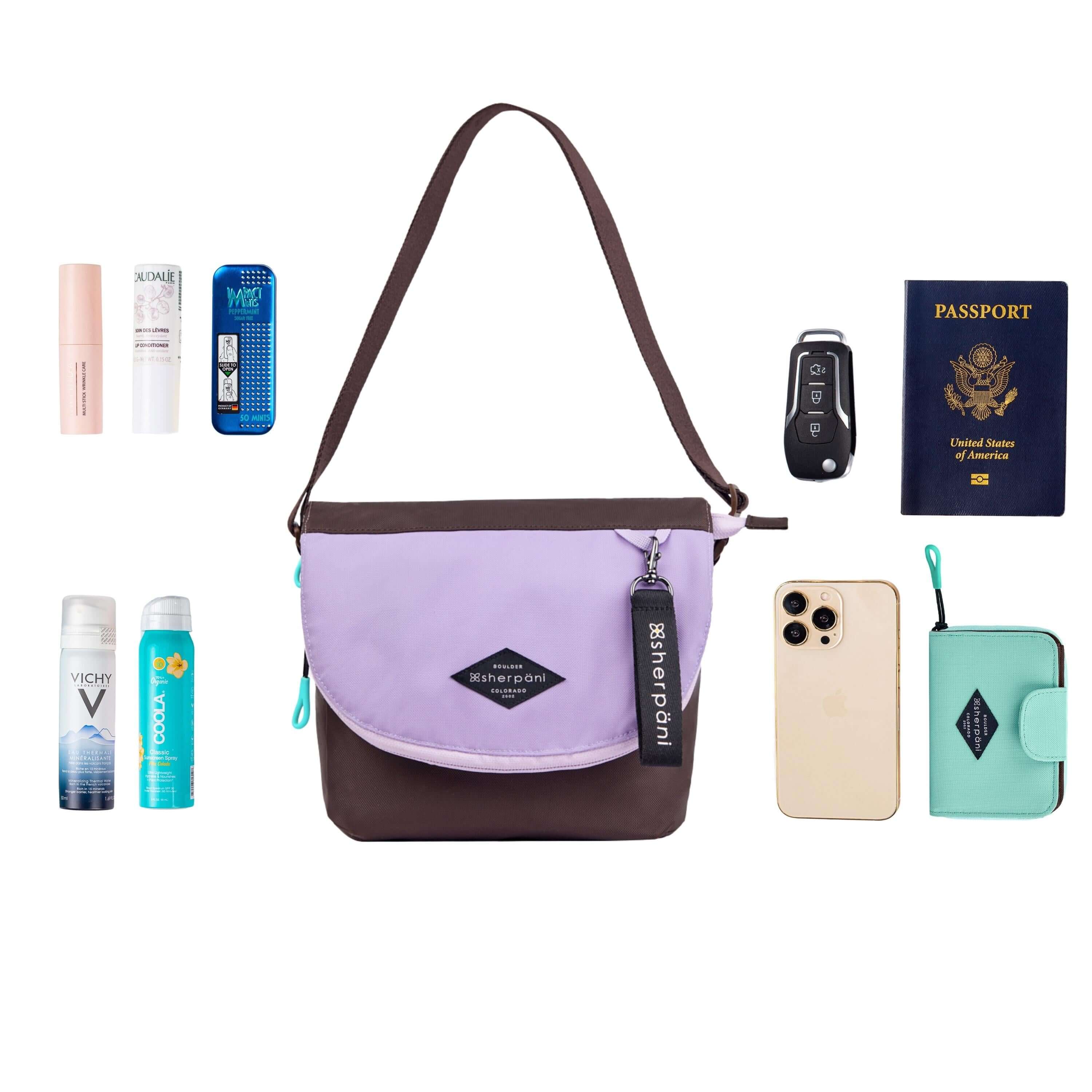 Top view of example items to fill the bag. Sherpani crossbody, the Milli in Lavender, lies in the center. It is surrounded by an assortment of items: skincare products, sunscreen, beauty spray, car key, passport, phone and Sherpani travel accessory the Barcelona in Seagreen.