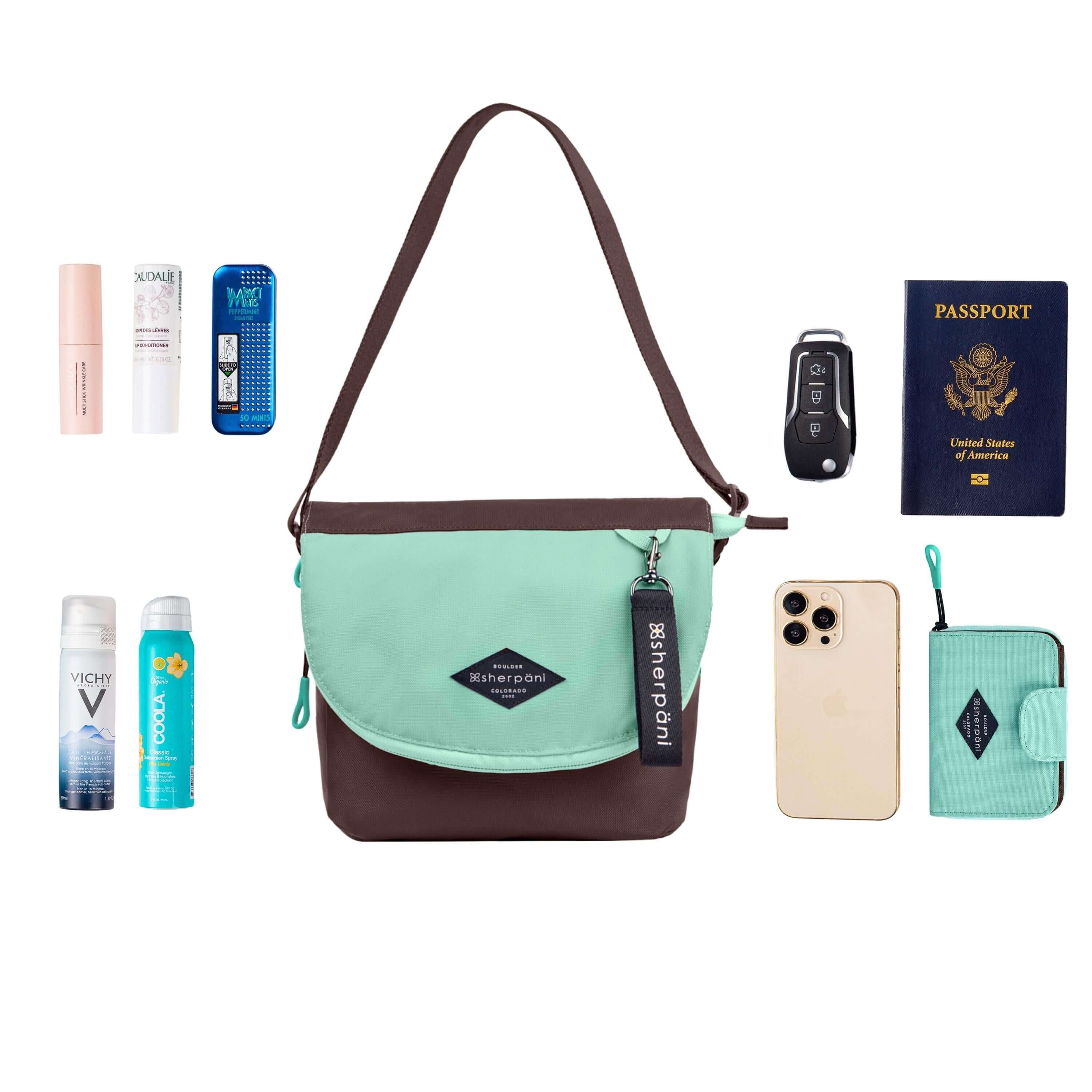 Top view of example items to fill the bag. Sherpani crossbody, the Milli in Seagreen, lies in the center. It is surrounded by an assortment of items: skincare products, sunscreen, beauty spray, car key, passport, phone and Sherpani travel accessory the Barcelona in Seagreen.
