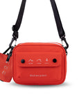 Flat front view of Sherpani crossbody, the Osaka in Poppy. The bag is red in color with a black daisy chain, accent buttons and adjustable/detachable crossbody strap. There is an external pocket on the front of the bag with a fold over flap. On the flap are white graphics of mountains, a wave and a pine tree above white text that reads "Open Your Eyes." The bag comes with a coin purse that has matching graphics and "Open Your Eyes" text.