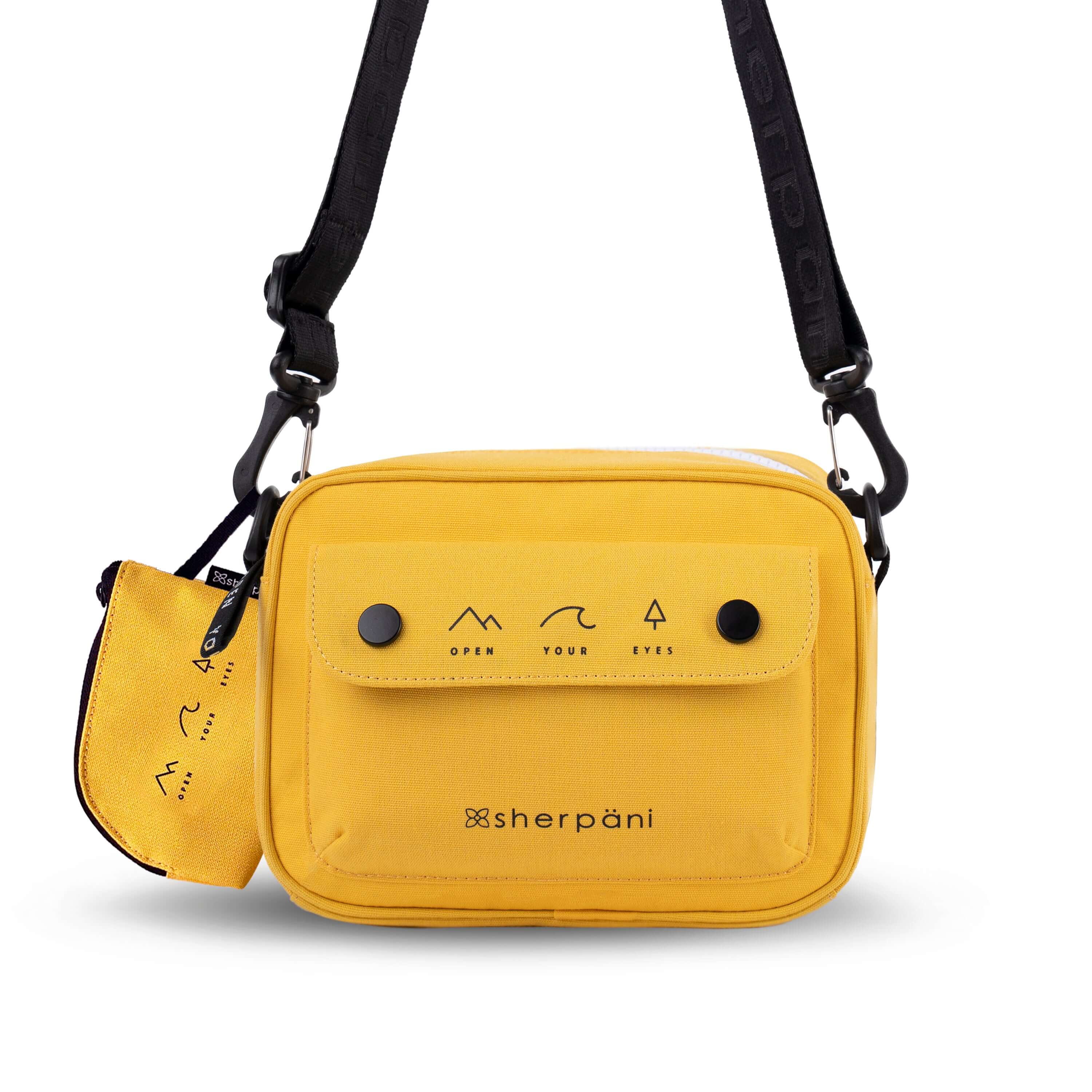 Flat front view of Sherpani crossbody, the Osaka in Sunflower. The bag is yellow in color with a black daisy chain, accent buttons and adjustable/detachable crossbody strap. There is an external pocket on the front of the bag with a fold over flap. On the flap are black graphics of mountains, a wave and a pine tree above black text that reads &quot;Open Your Eyes.&quot; The bag comes with a coin purse that has matching graphics and &quot;Open Your Eyes&quot; text.