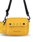Flat front view of Sherpani crossbody, the Osaka in Sunflower. The bag is yellow in color with a black daisy chain, accent buttons and adjustable/detachable crossbody strap. There is an external pocket on the front of the bag with a fold over flap. On the flap are black graphics of mountains, a wave and a pine tree above black text that reads "Open Your Eyes." The bag comes with a coin purse that has matching graphics and "Open Your Eyes" text.