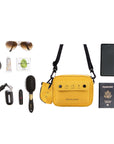 Top view of example items to fill the bag. Sherpani crossbody, the Osaka in Sunflower, lies in the center. It is surrounded by an assortment of items: sunglasses, hair tie, hand lotion, gum, car key, lipstick, hairbrush, phone and passport.