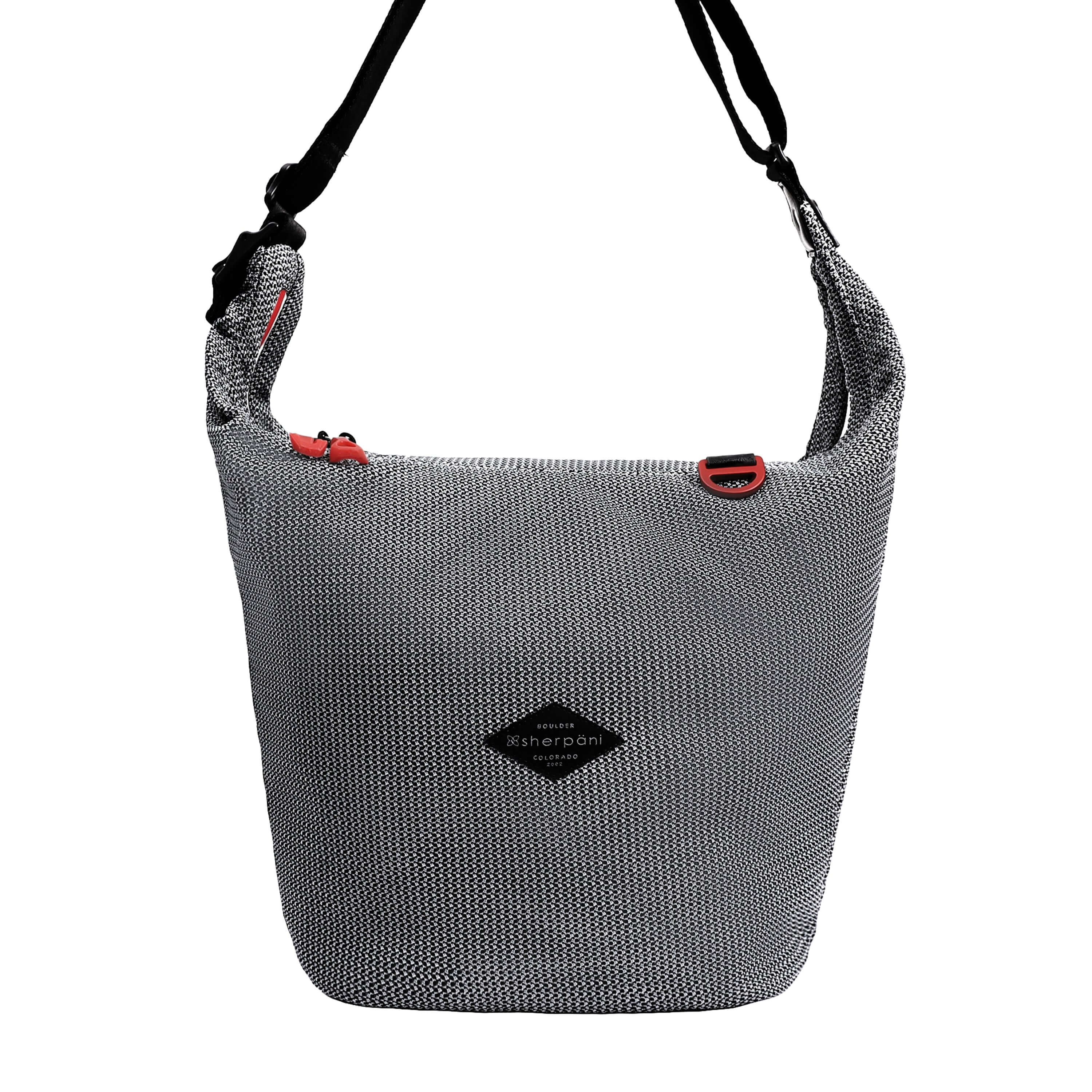 Flat front view of Sherpani mesh crossbody, the Payton. The bag has a black and white mesh pattern and features red pops of color on the accent buckle and easy-pull zipper. It has a black adjustable crossbody strap with a cam buckle.