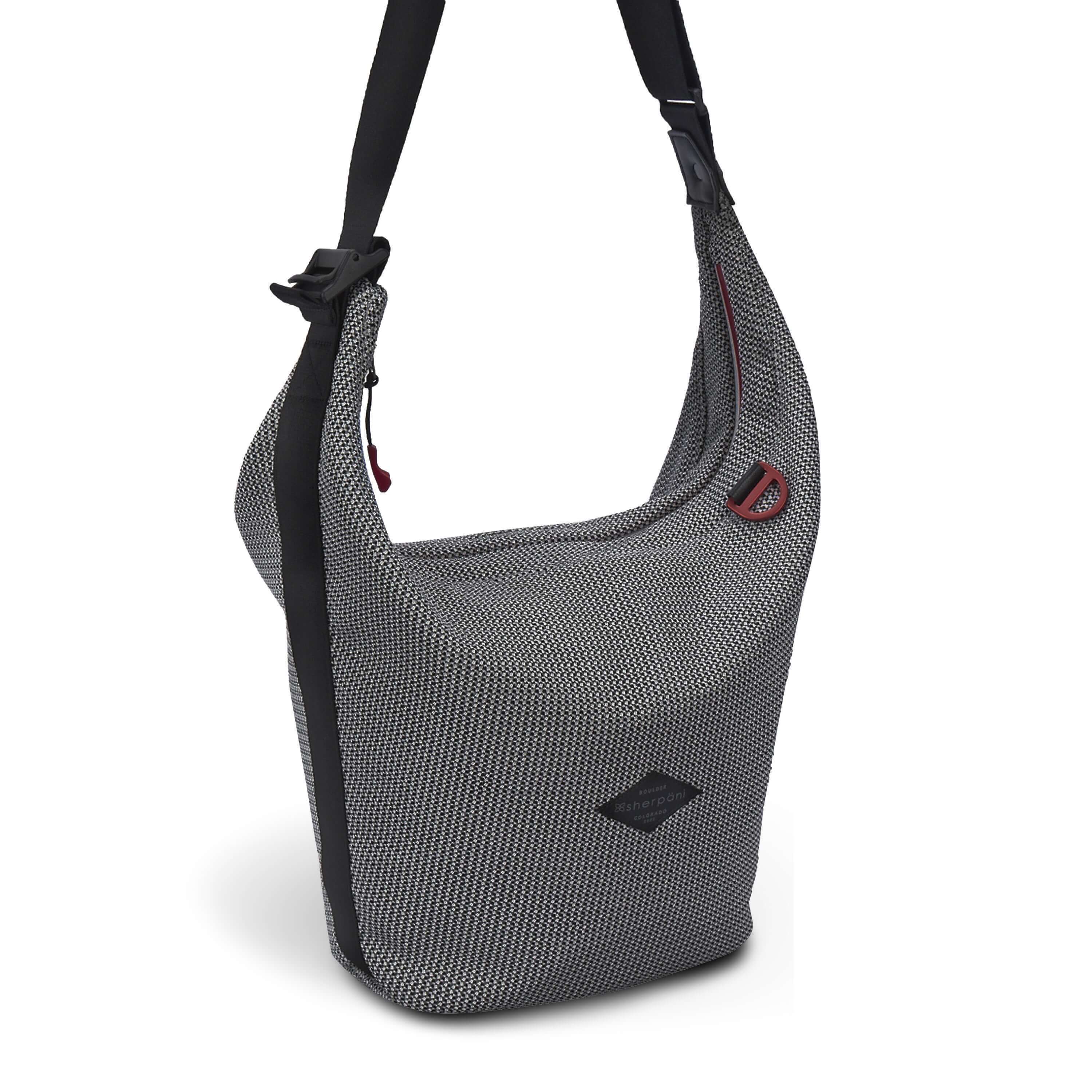 Angled front view of Sherpani mesh crossbody, the Payton. The bag has a black and white mesh pattern and features red pops of color on the accent buckle and easy-pull zipper. It has a black adjustable crossbody strap with a cam buckle.