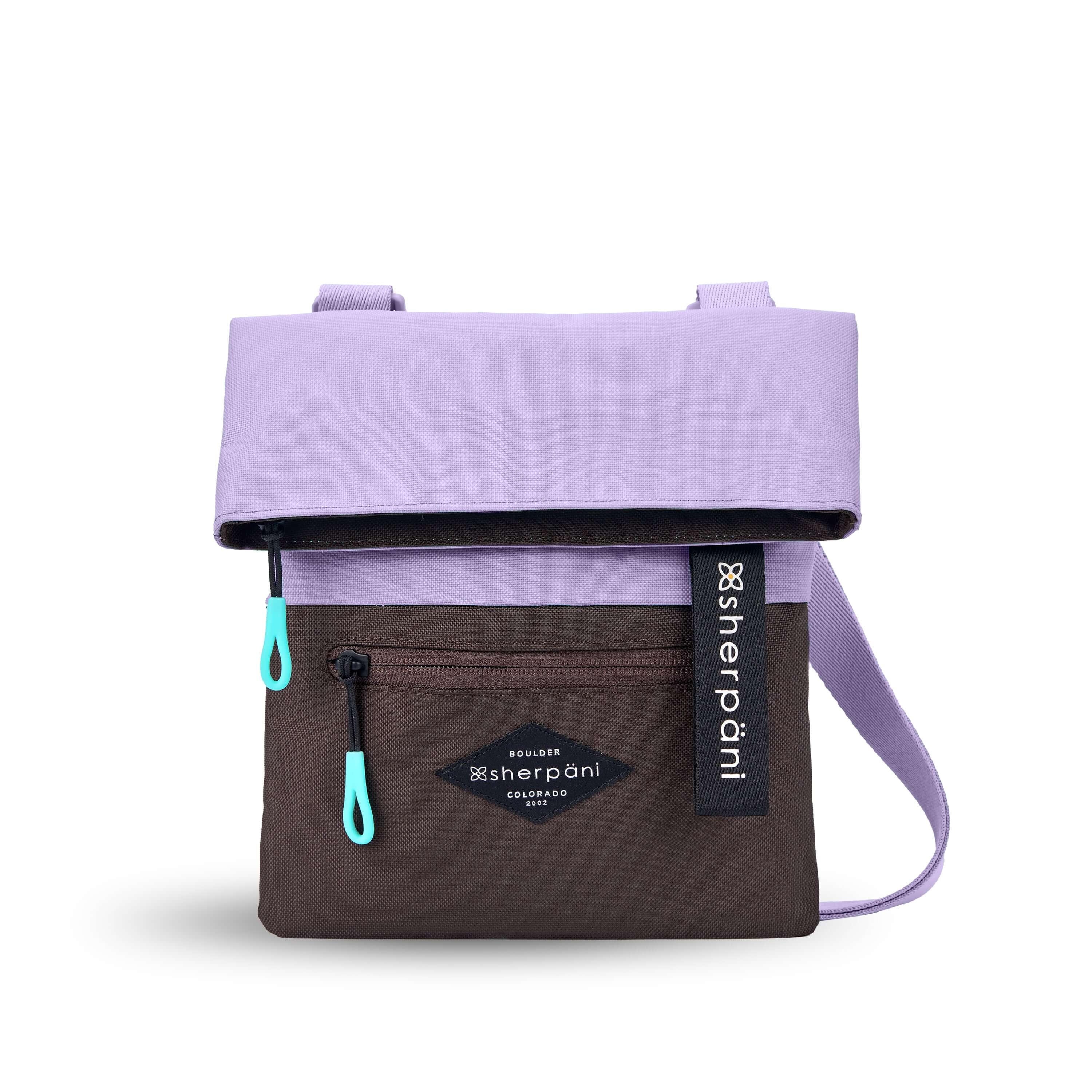 Flat front view of Sherpani crossbody, the Pica in Lavender. The bag is two toned: the top half is lavender and the bottom half is brown. There is an external zipper pocket on the front panel. Easy-pull zippers are accented in aqua. The top of the bag folds over creating a signature look. A branded Sherpani keychain is clipped to the upper right corner. The bag has an adjustable crossbody strap.