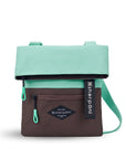 Flat front view of Sherpani crossbody, the Pica in Seagreen. The bag is two toned: the top half is light green and the bottom half is brown. There is an external zipper pocket on the front panel. Easy-pull zippers are accented in light green. The top of the bag folds over creating a signature look. A branded Sherpani keychain is clipped to the upper right corner. The bag has an adjustable crossbody strap.