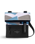 Flat front view of Sherpani crossbody, the Pica in Summer Camo. The bag is two toned: the top half is a camouflage pattern of light blue, gray and white and the bottom half is black. There is an external zipper pocket on the front panel. Easy-pull zippers are accented in black. The top of the bag folds over creating a signature look. A branded Sherpani keychain is clipped to the upper right corner. The bag has an adjustable crossbody strap.