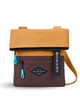 Flat front view of Sherpani crossbody, the Pica in Sundial. The bag is two toned: the top half is burnt yellow and the bottom half is brown. There is an external zipper pocket on the front panel. Easy-pull zippers are accented in aqua. The top of the bag folds over creating a signature look. A branded Sherpani keychain is clipped to the upper right corner. The bag has an adjustable crossbody strap.