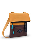Angled front view of Sherpani crossbody, the Pica in Sundial. The bag is two toned: the top half is burnt yellow and the bottom half is brown. There is an external zipper pocket on the front panel. Easy-pull zippers are accented in aqua. The top of the bag folds over creating a signature look. A branded Sherpani keychain is clipped to the upper right corner. The bag has an adjustable crossbody strap.