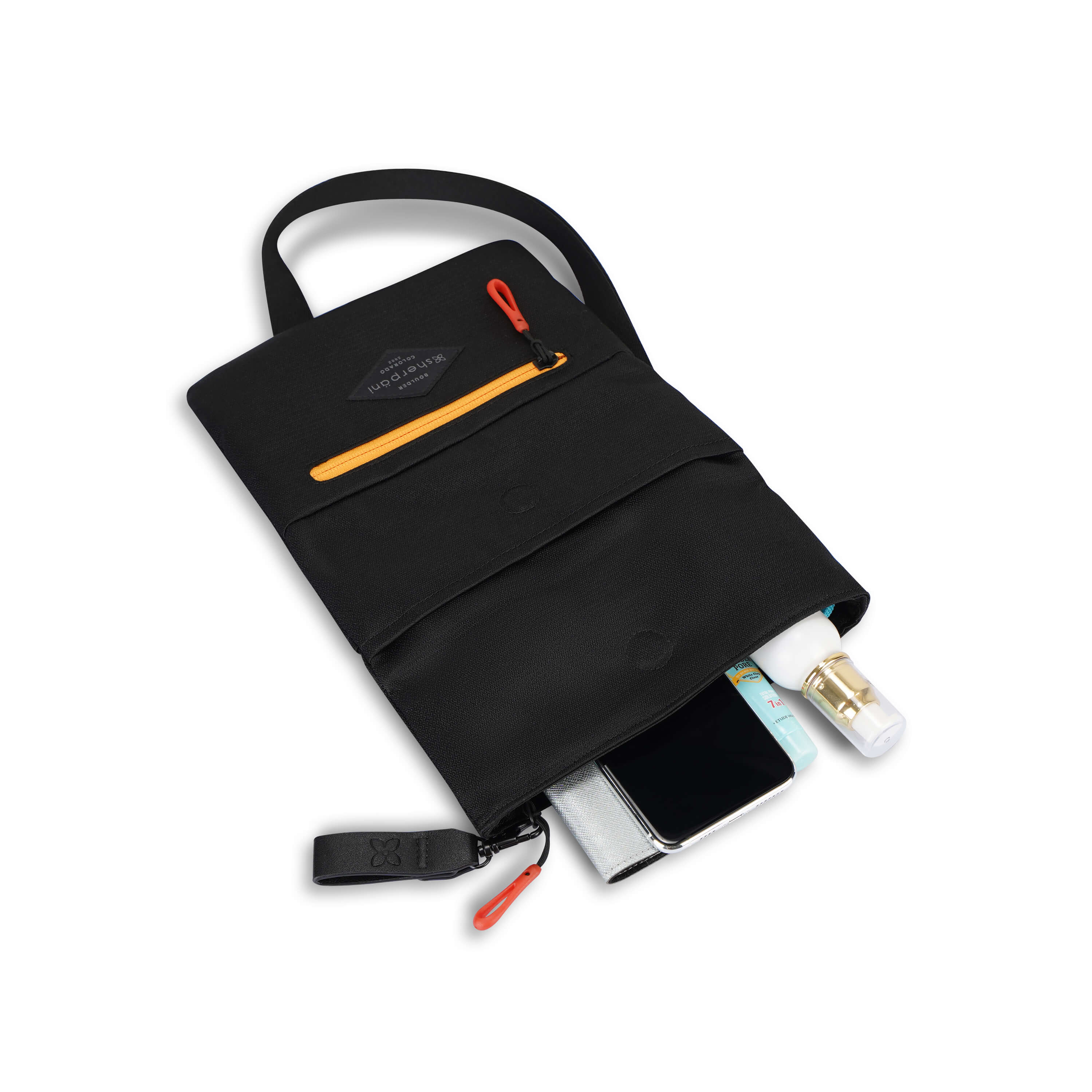 Top view of Sherpani crossbody, the Pica in Chromatic. The bag lies on the ground with the following items peaking out of it: spray bottle, sunscreen, phone and wallet.