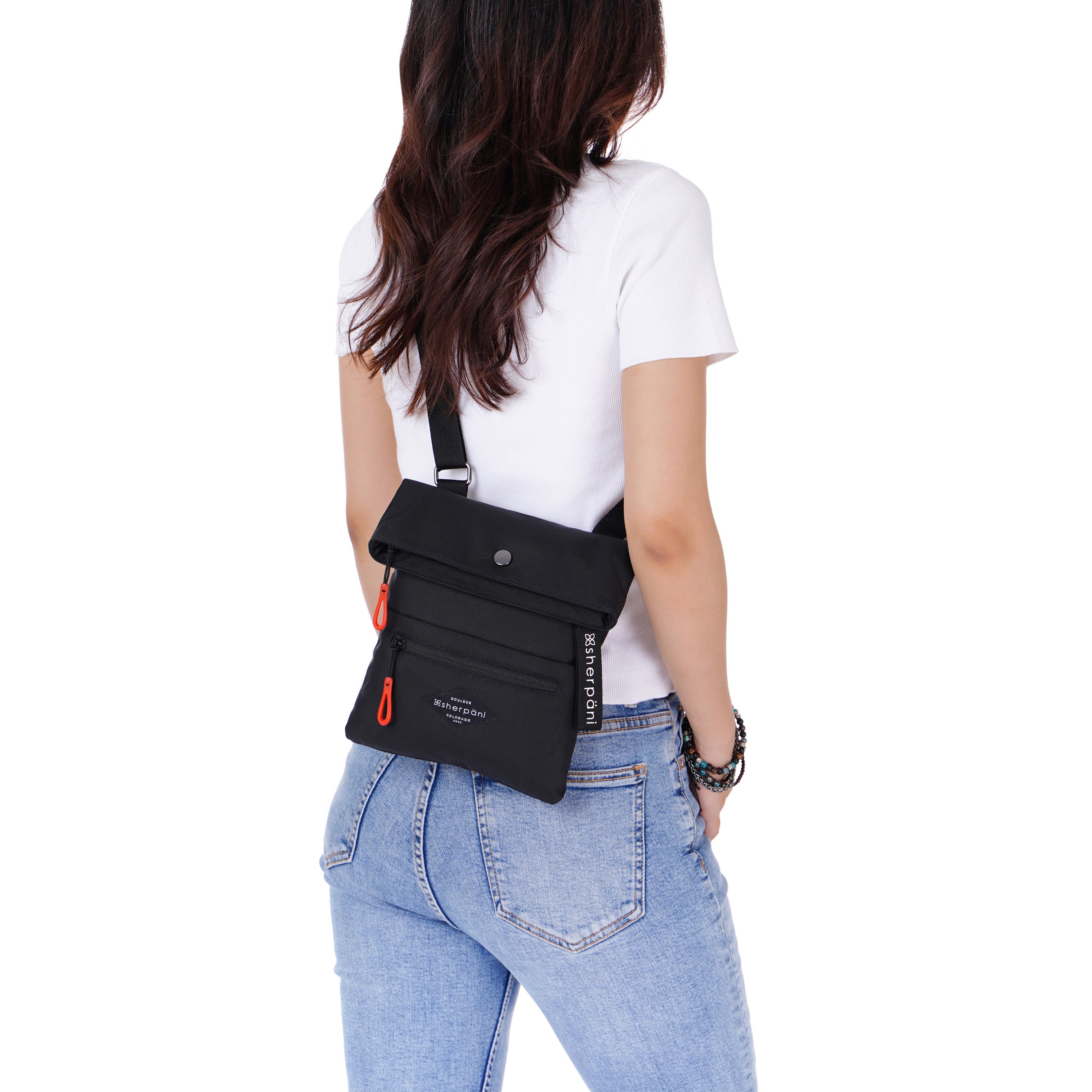 Close up view of a dark haired model facing away from the camera. She is wearing a white tee shirt and jeans. She carries Sherpani crossbody, the Pica in Raven, as a crossbody. 