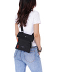 Close up view of a dark haired model facing away from the camera. She is wearing a white tee shirt and jeans. She carries Sherpani crossbody, the Pica in Raven, as a crossbody.