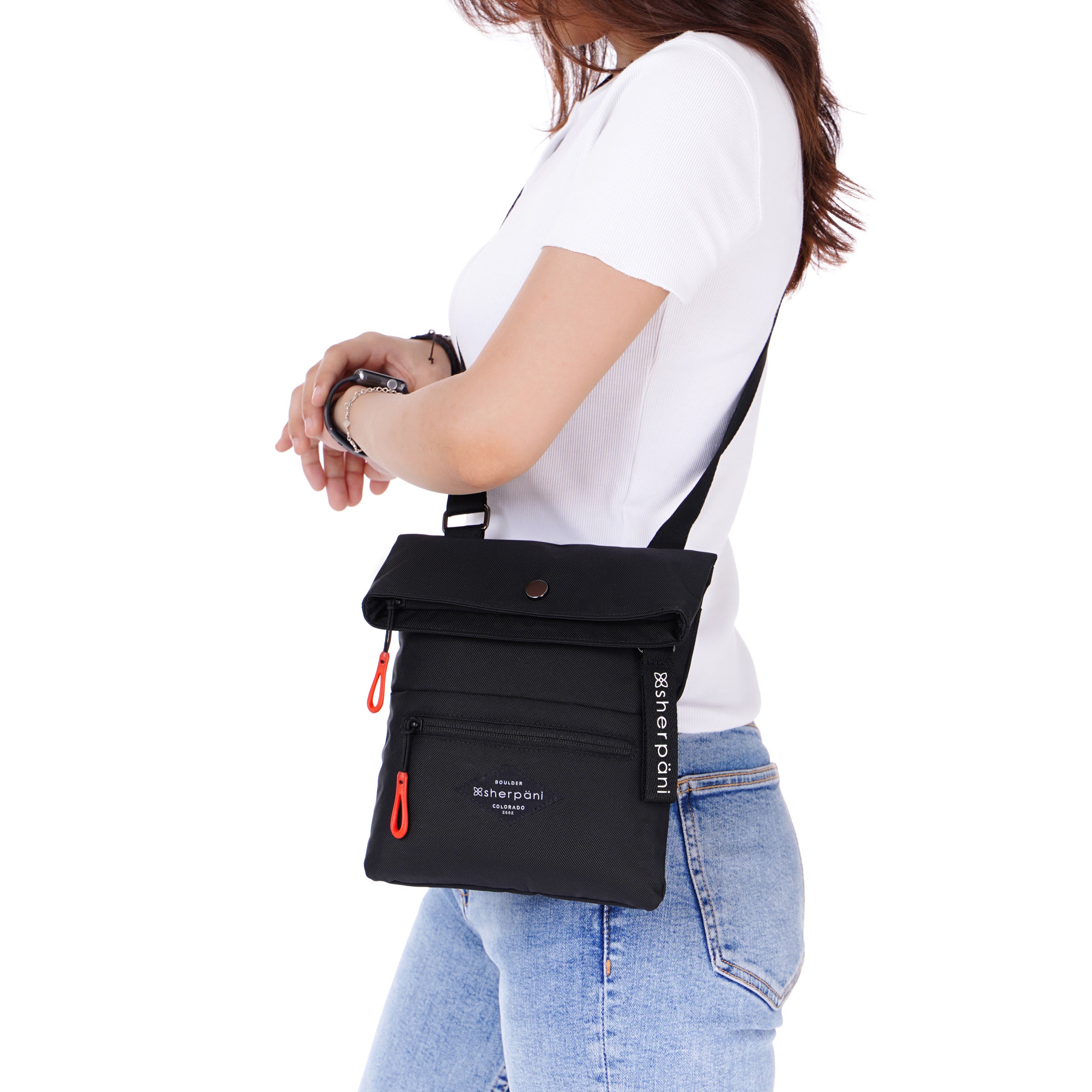 Close up view of a red haired model facing the side. She is wearing a white tee shirt and jeans. She carries Sherpani crossbody, the Pica in Raven, as a crossbody.