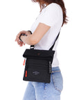 Close up view of a red haired model facing the side. She is wearing a white tee shirt and jeans. She carries Sherpani crossbody, the Pica in Raven, as a crossbody.