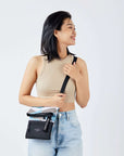 Close up view of a dark haired model facing the camera and smiling over her left shoulder. She is wearing a tan crop to and jeans. She carries Sherpani crossbody, the Pica in Summer Camo, as a crossbody.