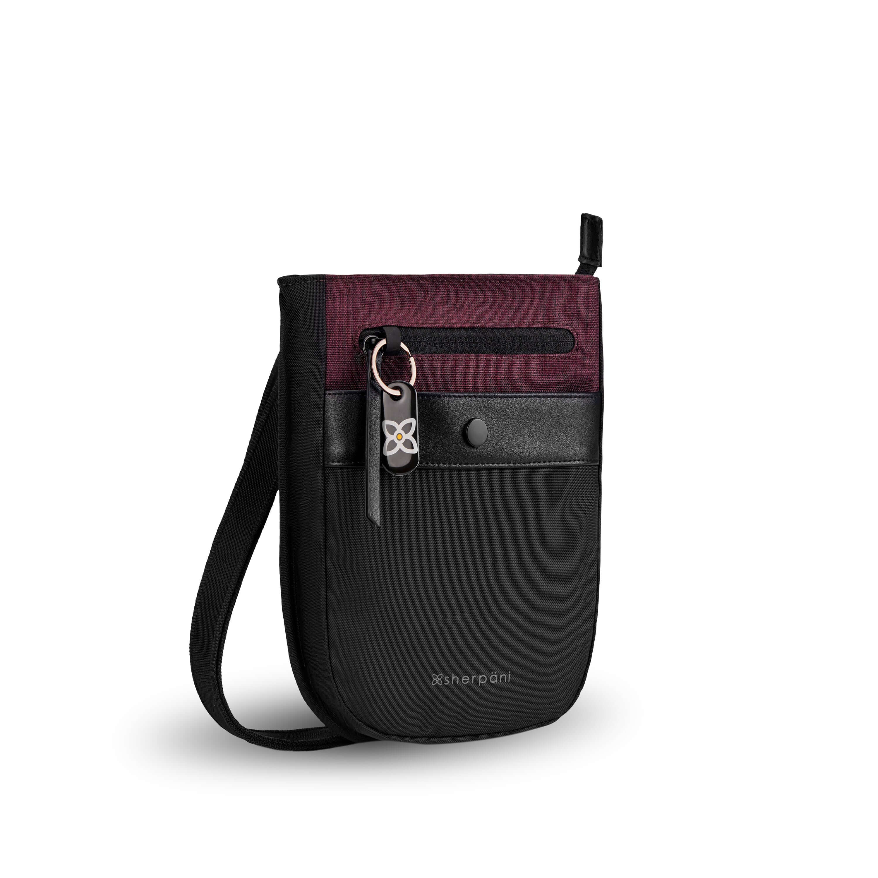 Angled front view of Sherpani’s Anti-Theft bag, the Prima AT in Merlot, with vegan leather accents in black. There is an external pouch on the front of the bag that sits below a locking zipper compartment, which has a ReturnMe tag clipped to it. The bag features an adjustable crossbody strap.