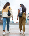 Two friends walk side-by-side, each carrying Sherpani Anti-Theft crossbody purse, the Prima over their shoulder.