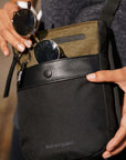 Close up view of a model's hands putting sunglasses into the front pocket of Sherpani's Anti-Theft bag the Prima AT in Loden.