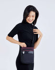 Close up view of a dark haired smiling down at her bag. She is wearing a black dress and Sherpani's Anti-Theft crossbody the Prima AT in Merlot.