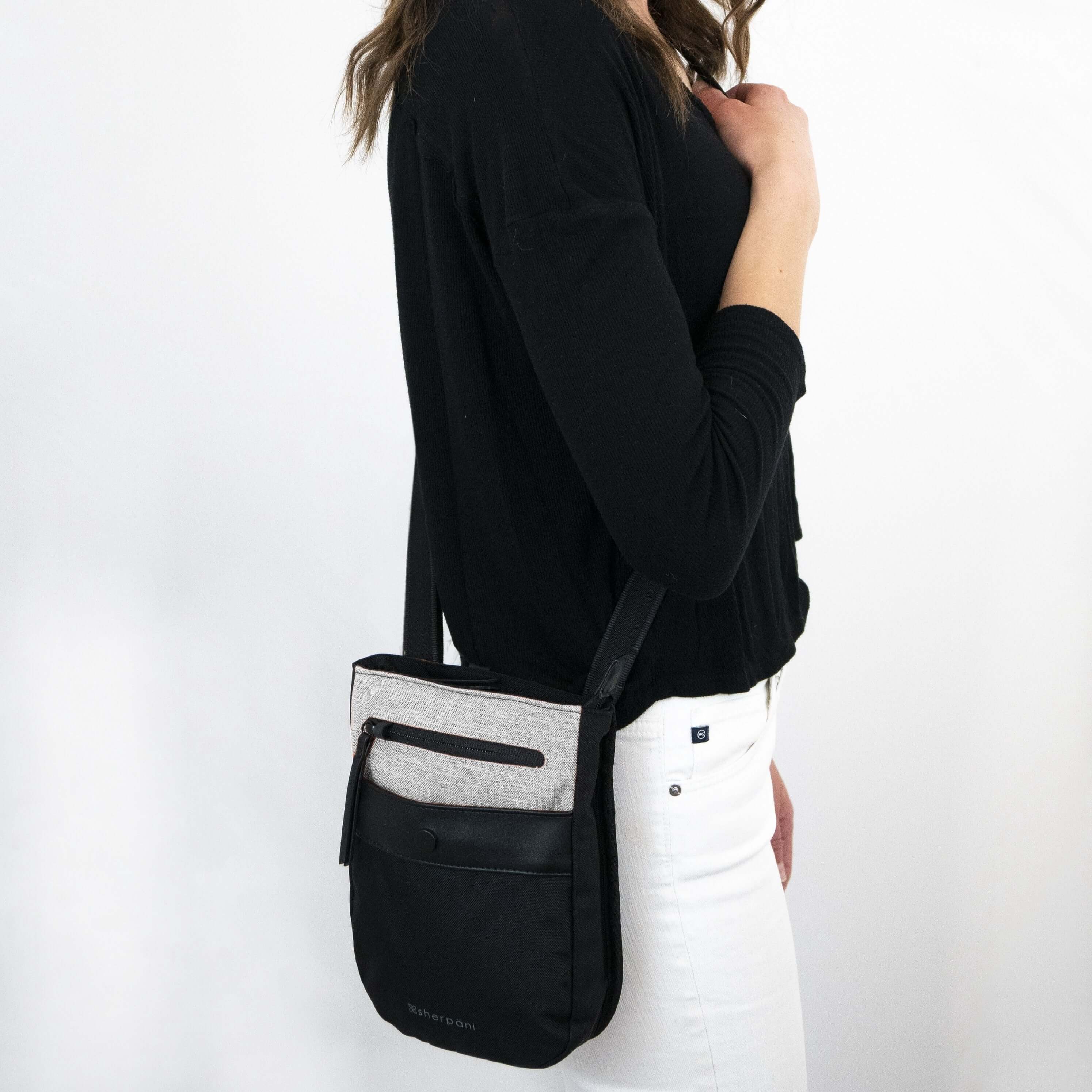 Close up view of a brown haired model facing the side. She is wearing a black shirt, white jeans and Sherpani&#39;s Anti-Theft crossbody the Prima AT in Sterling.