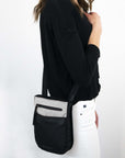Close up view of a brown haired model facing the side. She is wearing a black shirt, white jeans and Sherpani's Anti-Theft crossbody the Prima AT in Sterling.