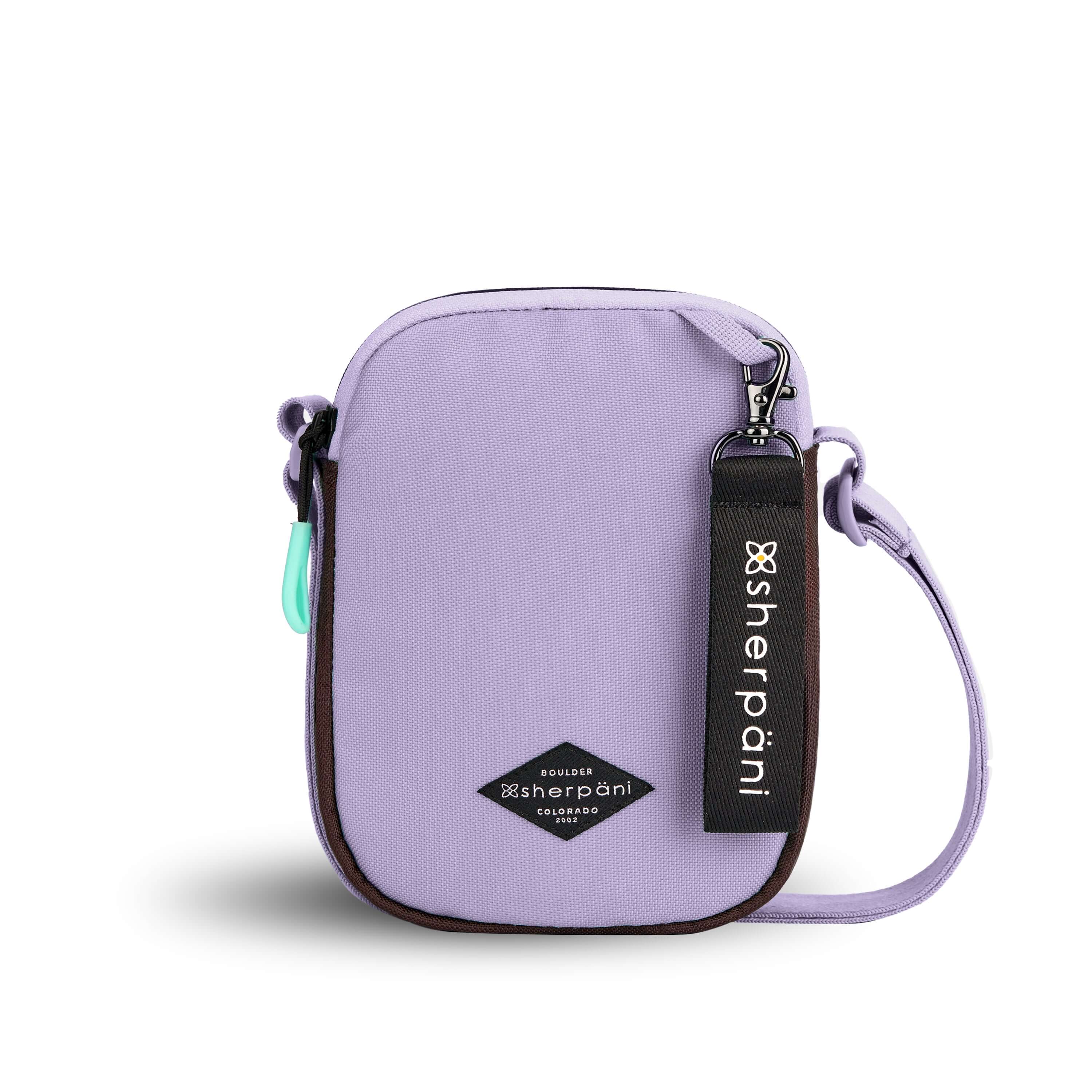 Flat front view of Sherpani crossbody, the Rogue in Lavender. The bag is two toned: the front is lavender and the back is brown. The main zipper compartment features an easy-pull zipper accented in aqua. The bag has an adjustable crossbody strap. A branded Sherpani keychain is clipped to a fabric loop on the top right corner.