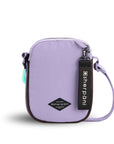 Flat front view of Sherpani crossbody, the Rogue in Lavender. The bag is two toned: the front is lavender and the back is brown. The main zipper compartment features an easy-pull zipper accented in aqua. The bag has an adjustable crossbody strap. A branded Sherpani keychain is clipped to a fabric loop on the top right corner.