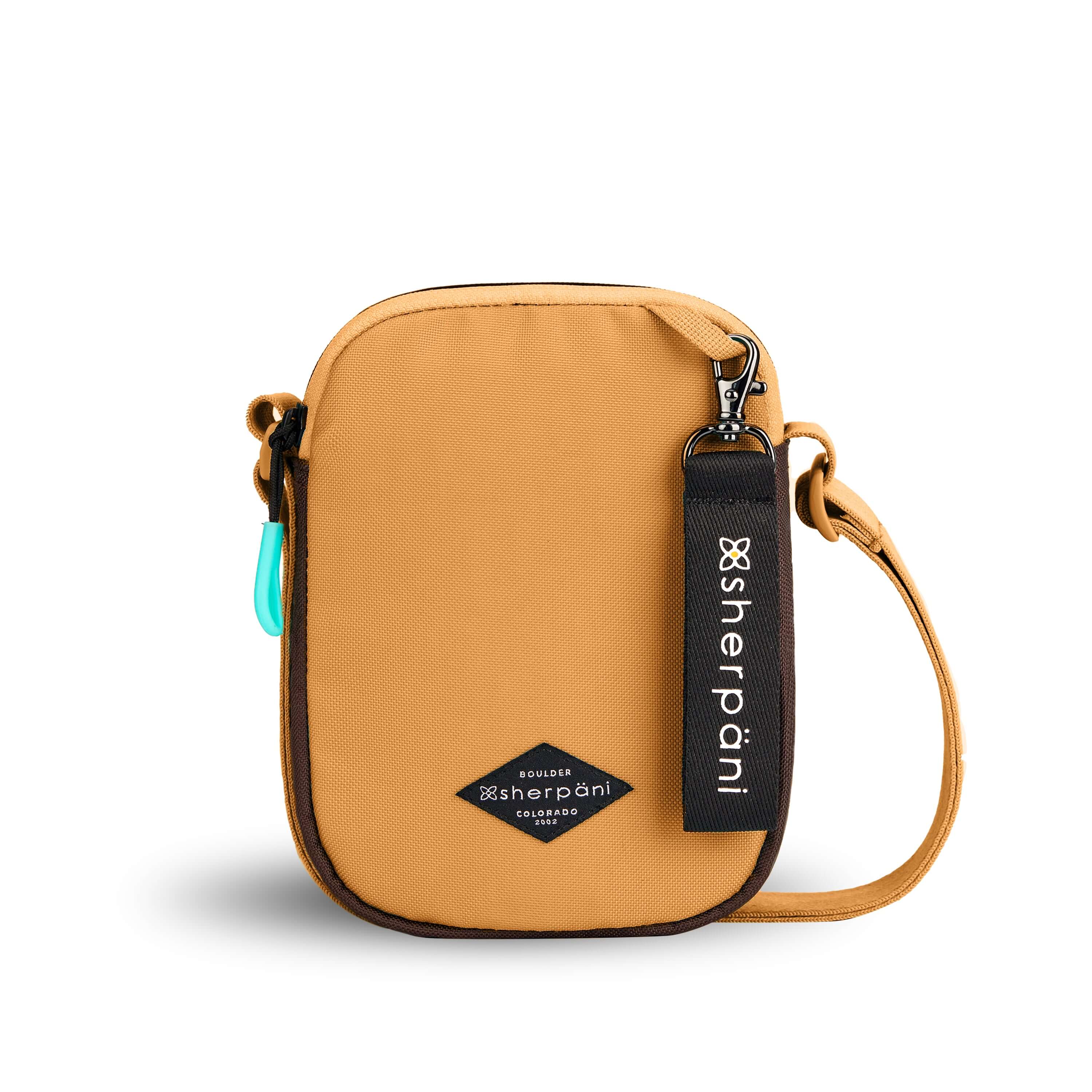 Flat front view of Sherpani crossbody, the Rogue in Sundial. The bag is two toned: the front is burnt yellow and the back is brown. The main zipper compartment features an easy-pull zipper accented in aqua. The bag has an adjustable crossbody strap. A branded Sherpani keychain is clipped to a fabric loop on the top right corner.