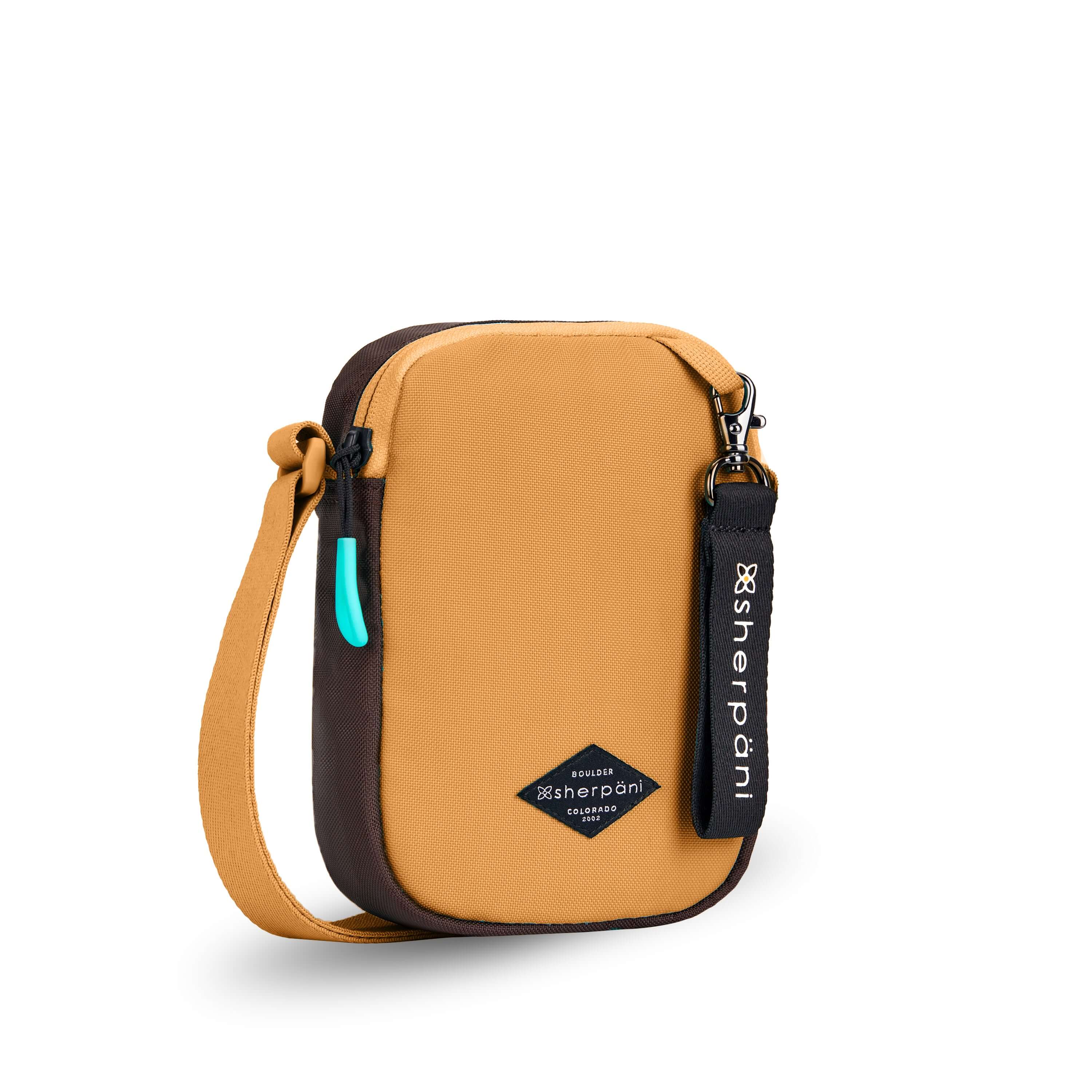 Angled front view of Sherpani crossbody, the Rogue in Sundial. The bag is two toned: the front is burnt yellow and the back is brown. The main zipper compartment features an easy-pull zipper accented in aqua. The bag has an adjustable crossbody strap. A branded Sherpani keychain is clipped to a fabric loop on the top right corner. #color_sundial