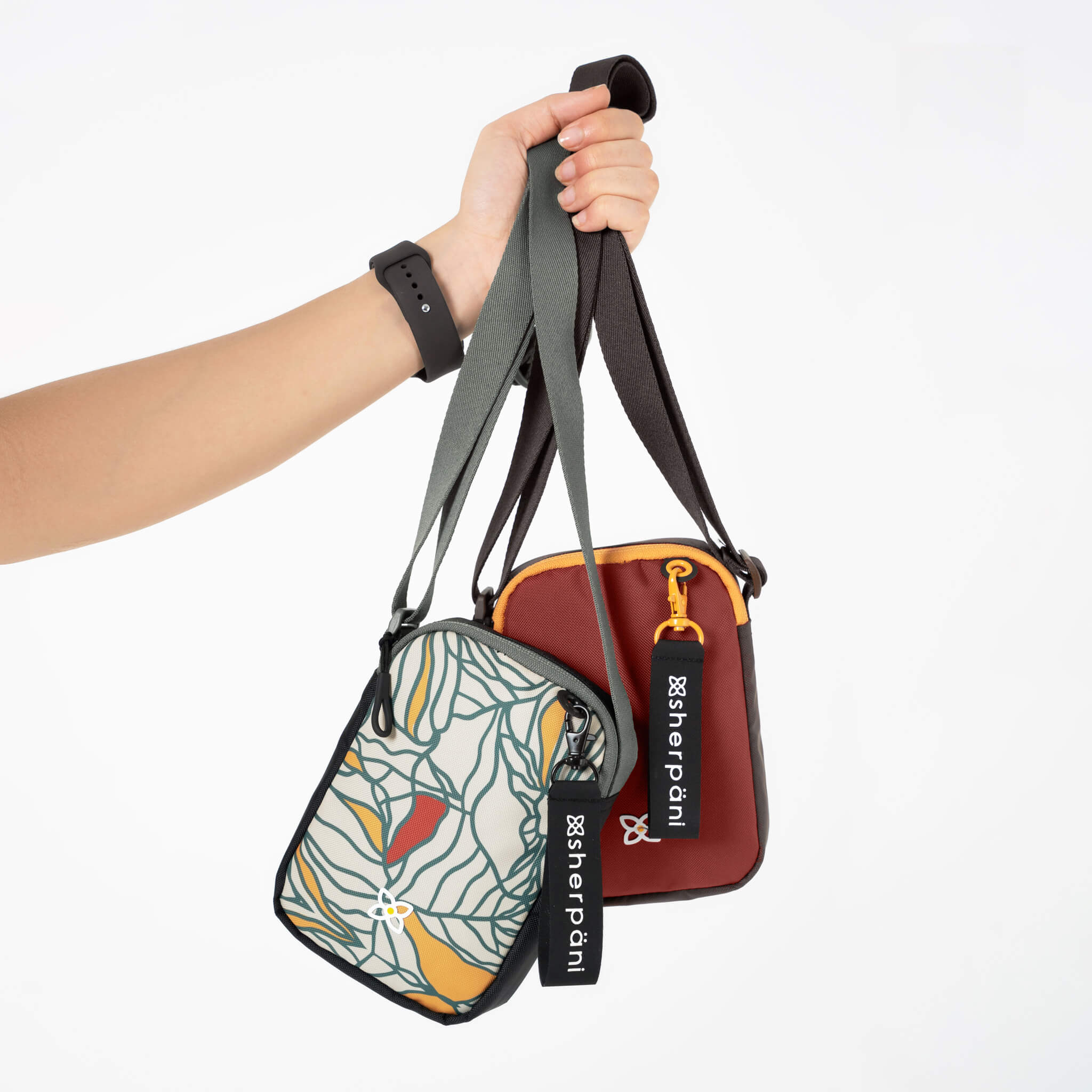 A woman&#39;s hand holds up two mini crossbody bags, the Rogue in Fiori and the Rogue in Cider.