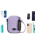 Top view of example items to fill the bag. Sherpani crossbody, the Rogue in Lavender, lies in the center. It is surrounded by an assortment of items: skincare products, sunscreen, beauty spray, mints, car key, passport, phone and Sherpani travel accessory the Barcelona in Seagreen.