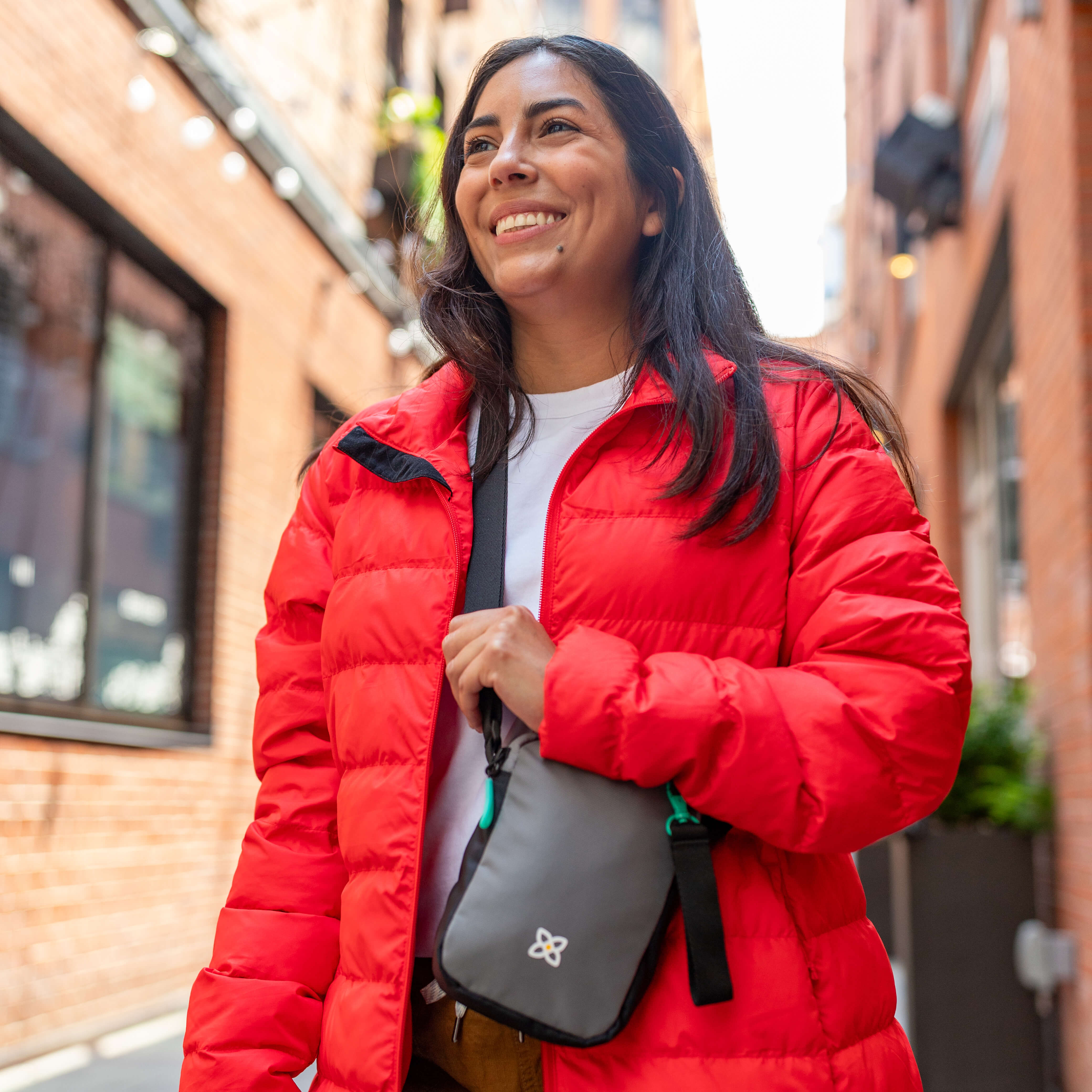 A woman standing outside and smiling. She is wearing Sherpani RFID travel bag, the Rogue in Moonstone. 