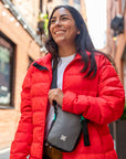 A woman standing outside and smiling. She is wearing Sherpani RFID travel bag, the Rogue in Moonstone.