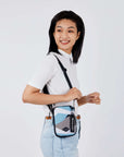 Close up view of a dark haired model facing the side and smiling over her right shoulder. She is wearing a white tee shirt and jeans. She carries Sherpani crossbody, the Rogue in Summer Camo, over her shoulder.