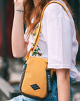 Close up view of a red haired woman outside. She is wearing a white shirt with flowers and jeans. She carries Sherpani crossbody, the Rogue in Sundial, over her shoulder.