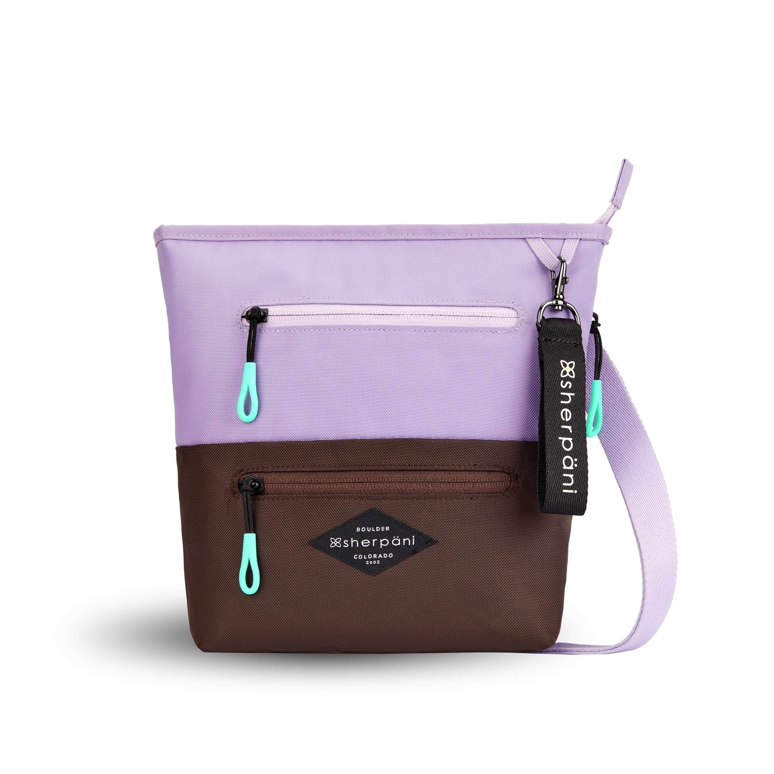 Flat front view of Sherpani’s crossbody, the Sadie, in Lavender. The top half of the bag is lavender and the bottom half of the bag is brown. It features two exterior zipper pockets on the front panel with easy-pull zippers accented in aqua. A Sherpani branded keychain is attached to a fabric loop in the upper right corner. It has an adjustable crossbody strap.