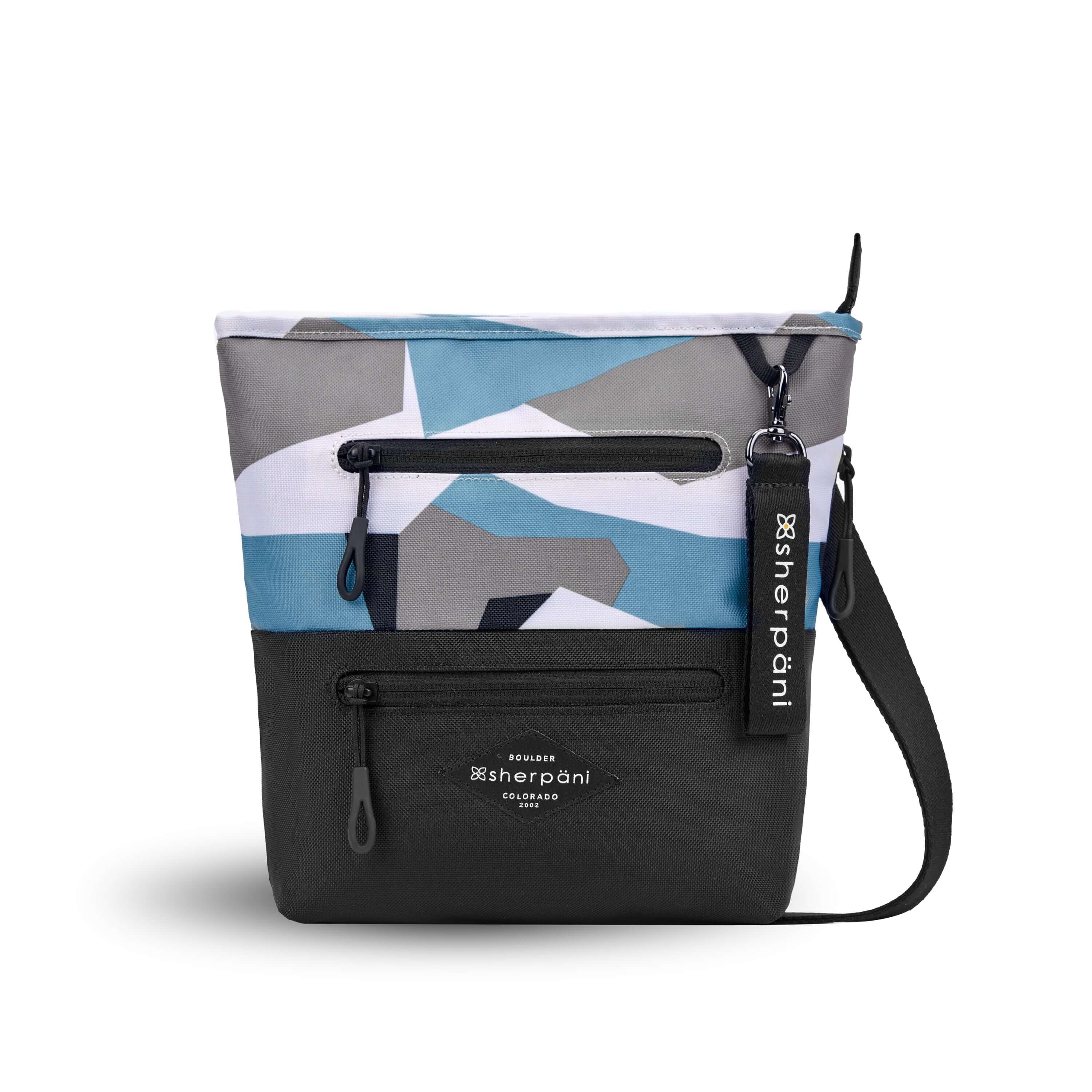 Flat front view of Sherpani’s crossbody, the Sadie, in Summer Camo. The top half of the bag is a camouflage pattern of white, gray and light blue, the bottom half of the bag is black. It features two exterior zipper pockets on the front panel with easy pull zippers accented in black. A Sherpani branded keychain is attached to a fabric loop in the upper right corner. It has an adjustable crossbody strap. 