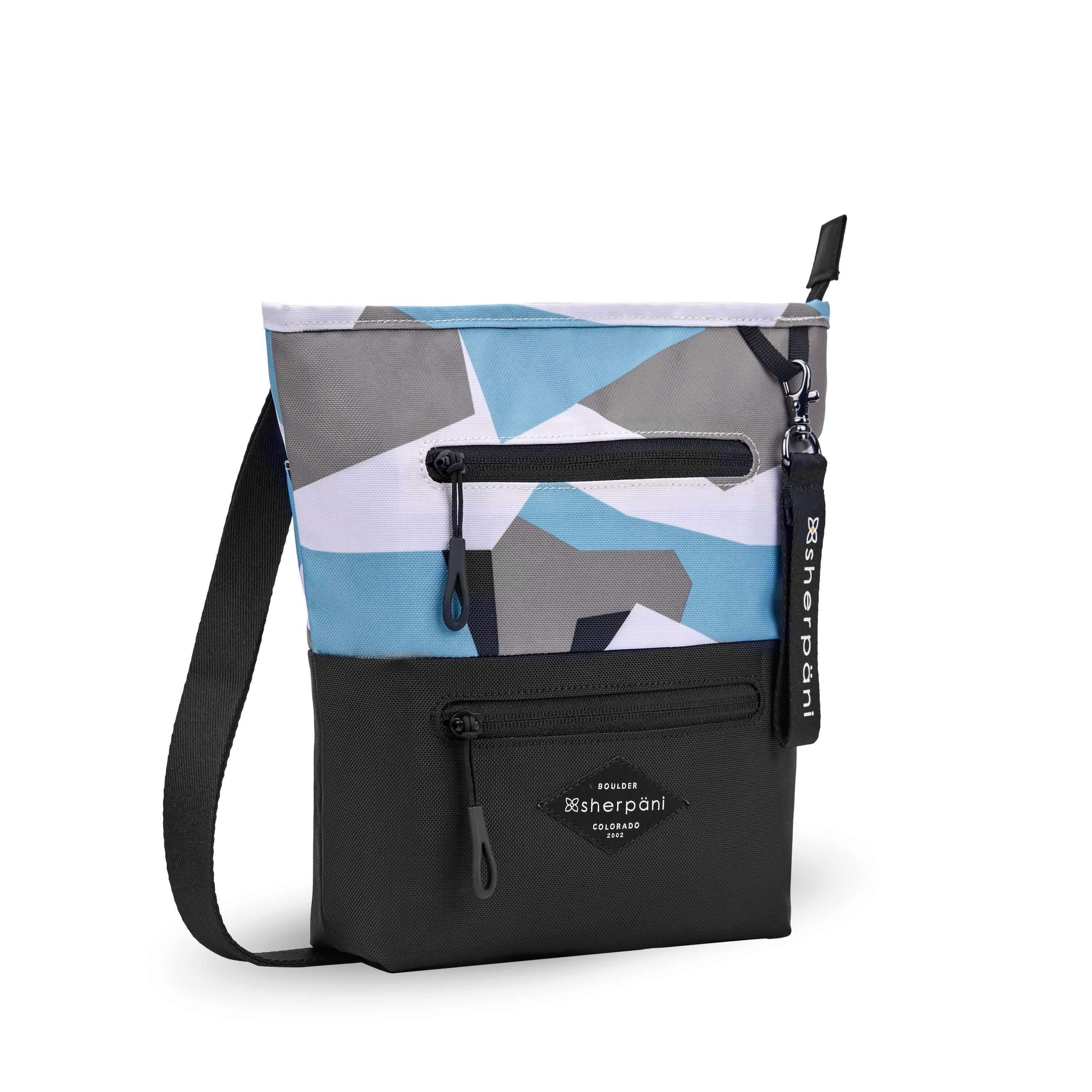 Angled front view of Sherpani’s crossbody, the Sadie, in Summer Camo. The top half of the bag is a camouflage pattern of white, gray and light blue, the bottom half of the bag is black. It features two exterior zipper pockets on the front panel with easy-pull zippers accented in black. A Sherpani branded keychain is attached to a fabric loop in the upper right corner. It has an adjustable crossbody strap.