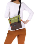 Close up view of a dark haired model facing away from the camera. She is wearing a white shirt and orange pants. She carries Sherpani crossbody, the Sadie in Cactus.