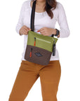Close up view of a brown haired model facing the camera. She is wearing a white shirt and orange pants. She is opening the main zipper compartment of Sherpani crossbody, the Sadie in Cactus.
