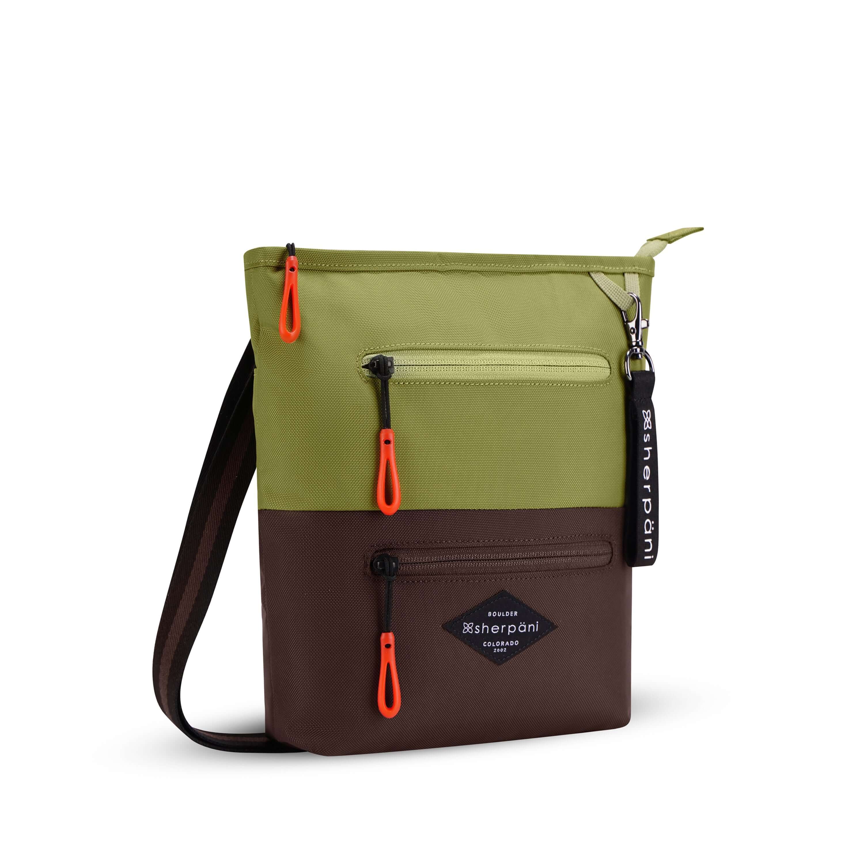 Angled front view of Sherpani's crossbody, the Sadie, in Cactus. The top half of the bag is green and the bottom half is brown. It features two exterior zipper pockets on the front panel with easy-pull zippers accented in red. A Sherpani branded keychain is attached to a fabric loop in the upper right corner. It has an adjustable crossbody strap. #color_cactus