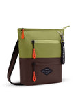 Angled front view of Sherpani's crossbody, the Sadie, in Cactus. The top half of the bag is green and the bottom half is brown. It features two exterior zipper pockets on the front panel with easy-pull zippers accented in red. A Sherpani branded keychain is attached to a fabric loop in the upper right corner. It has an adjustable crossbody strap.