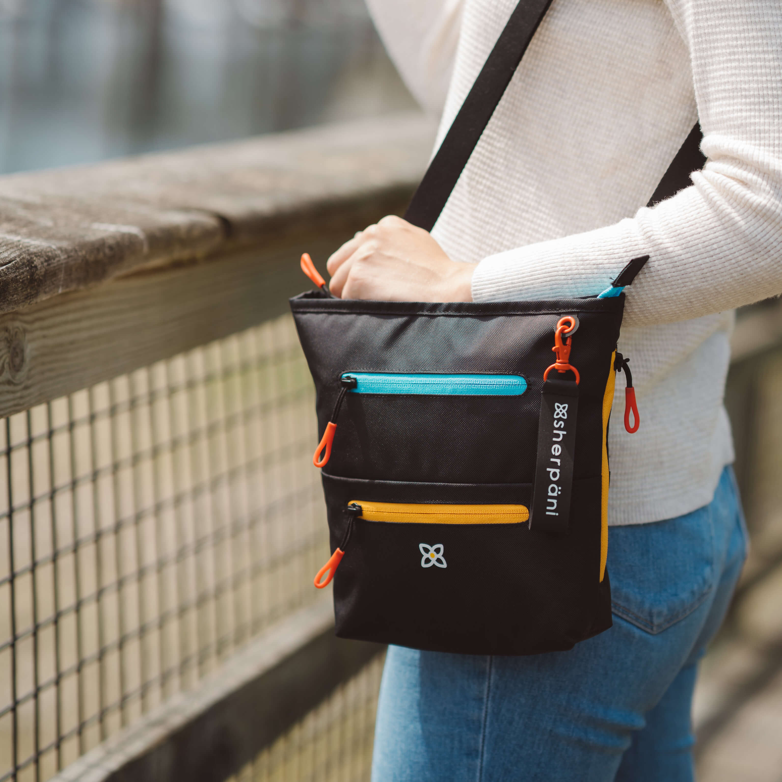 A woman standing outside. She is wearing Sherpani RFID blocking bag, the Sadie in Chromatic. 