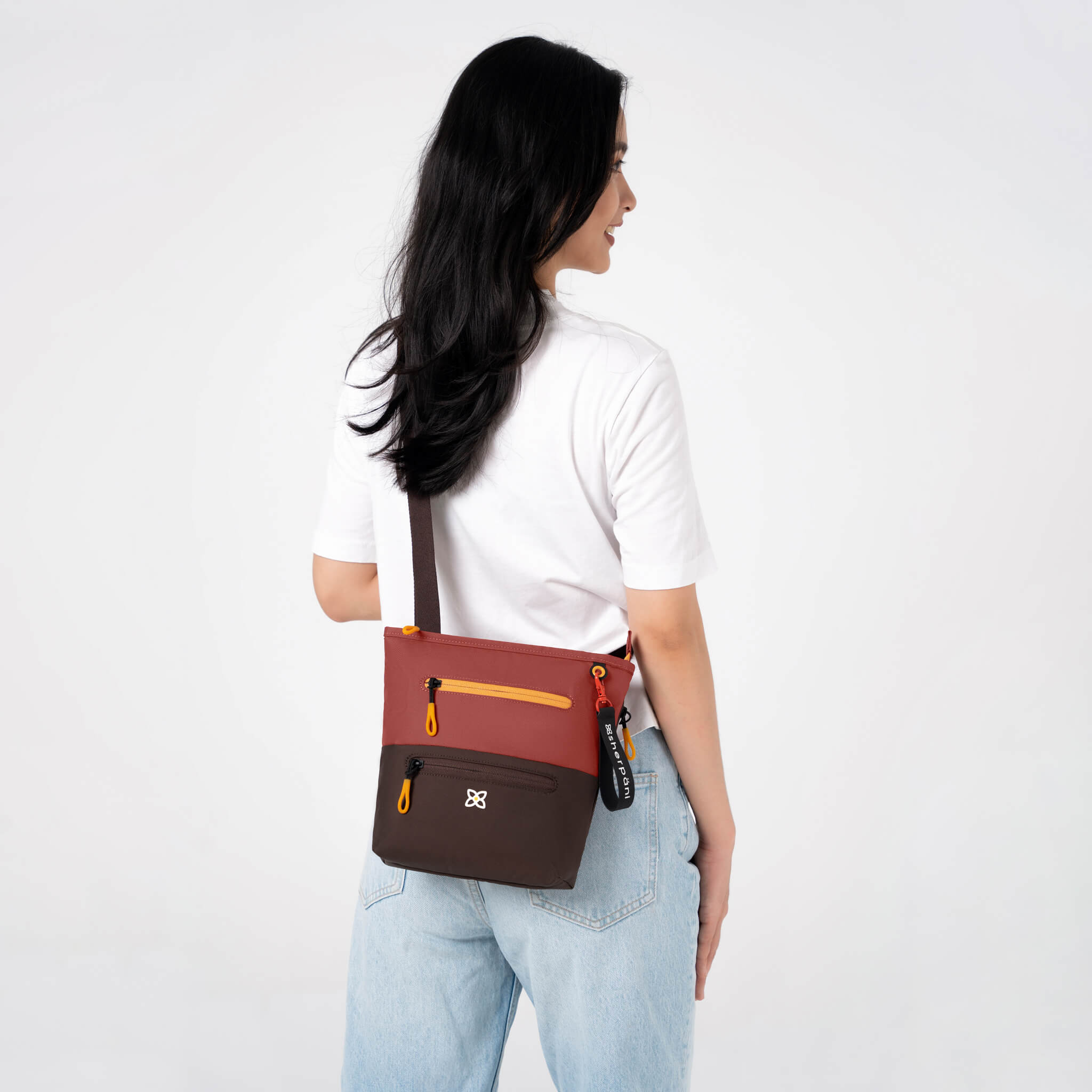 A model wearing Sherpani crossbody travel bag, the Sadie in Cider. 