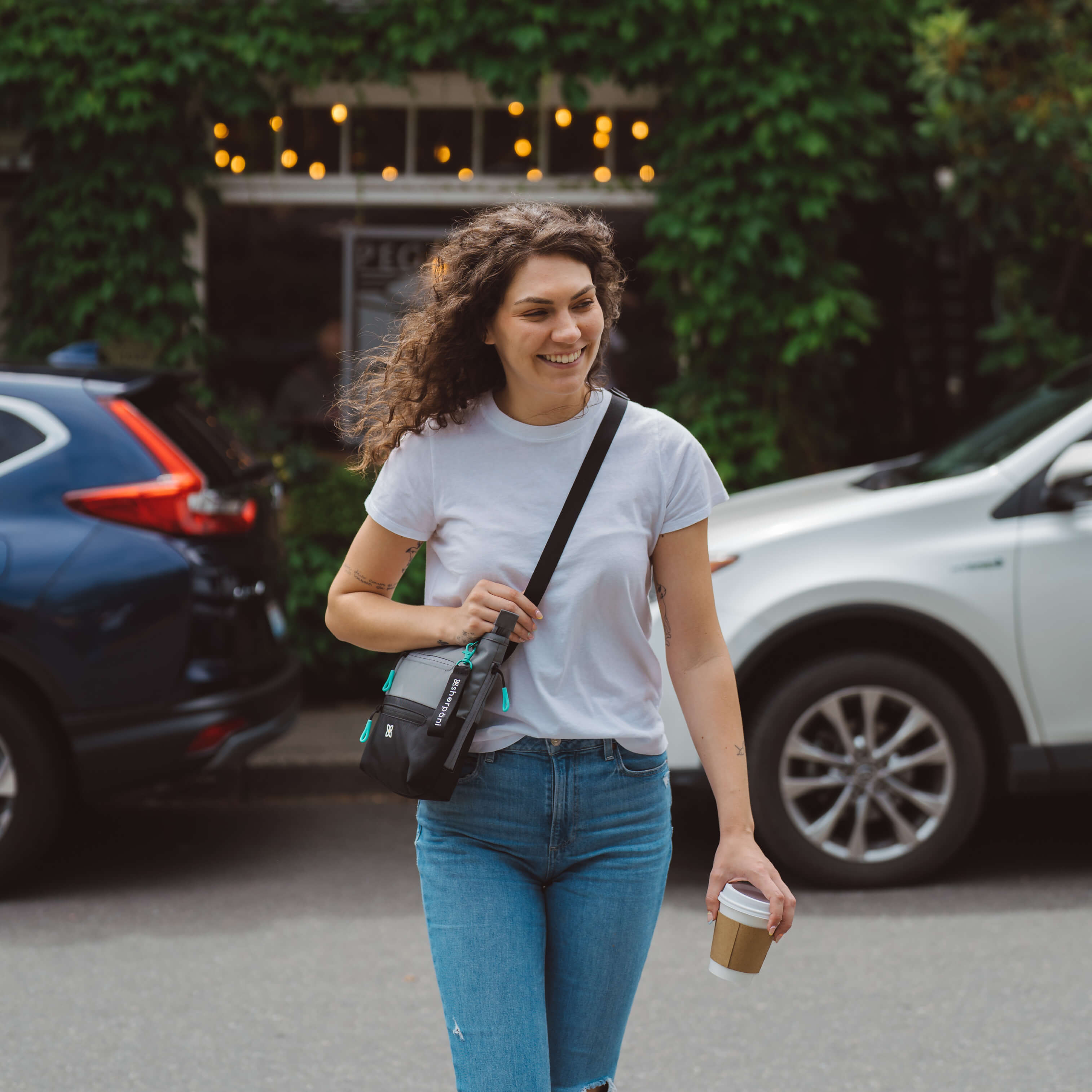 A woman walks down a street wearing Sherpani eco friendly handbag, the Sadie in Moonstone. 