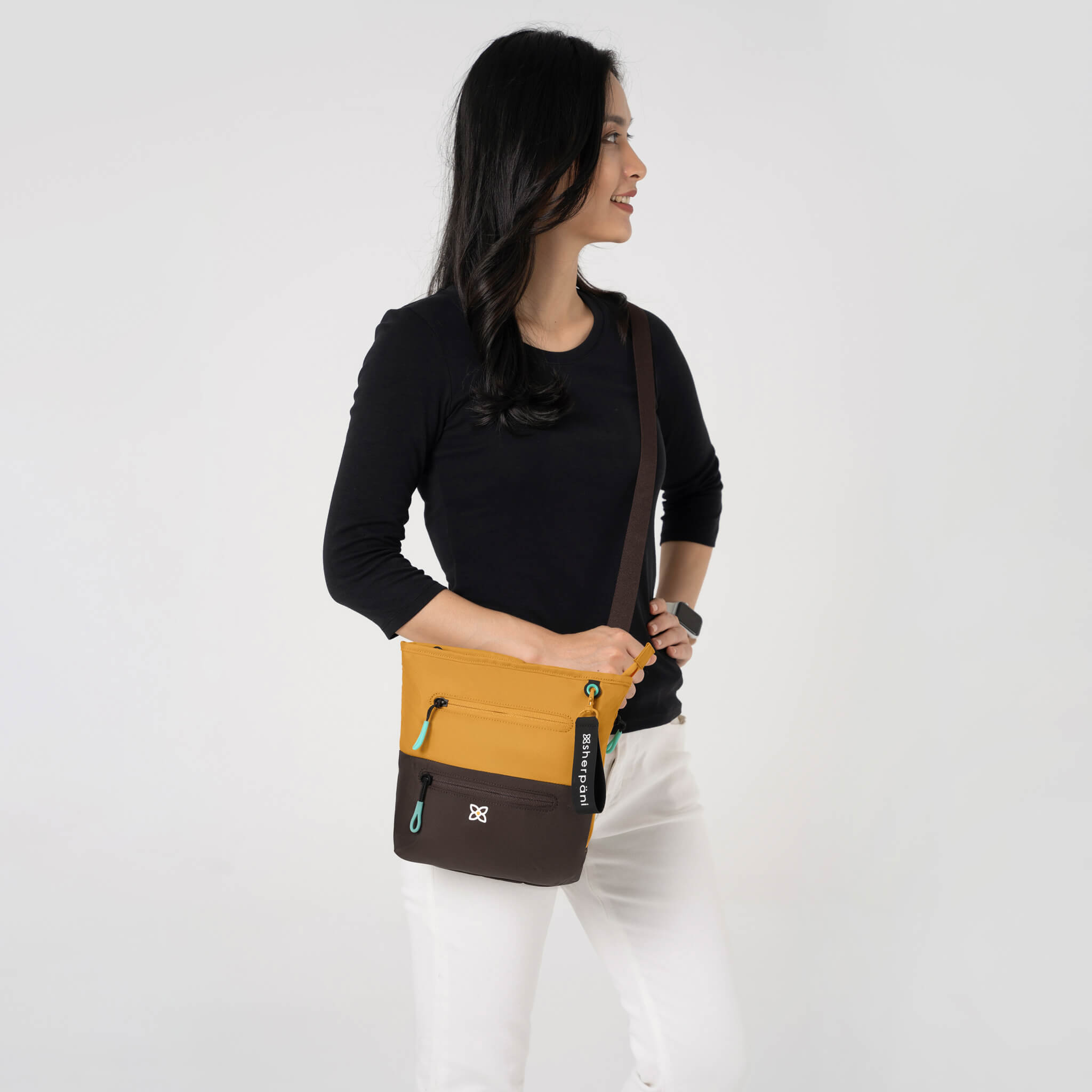 A model wearing Sherpani RFID protected crossbody travel purse, the Sadie in Sundial. 