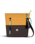 Flat front view of Sherpani crossbody travel bag, the Sadie in Sundial. Sadie features include two front zipper pockets, a discrete side pocket, detachable keychain, adjustable crossbody strap, back slip pocket and RFID blocking technology. The Sundial color is two-toned in yellow and dark brown with turquoise accents.